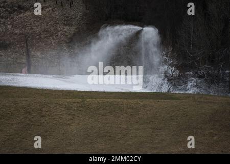 Schneelanze, die künstlichen Schnee auf Pisten und in Skigebieten mit grünem braunem Gras im Vordergrund im Winter produziert, ohne Schnee als Stockfoto