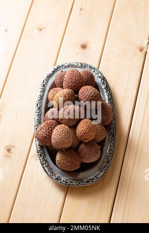 Ein Haufen Lychee-Früchte auf einem Metallteller, auf einem Holztisch, Nahaufnahme Stockfoto