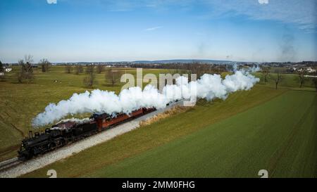 Drohnenansicht einer antiken Dampflok, Annäherung, Dampf blasen und Reisen auf dem Land Stockfoto