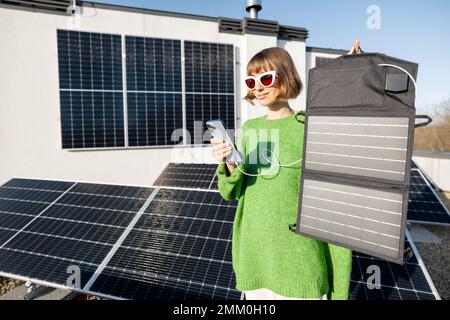 Frau lädt Handy von einem tragbaren Solarmodul Stockfoto