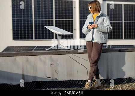 Frau benutzt Starlink Internet auf dem Dach mit Solarpaneelen Stockfoto