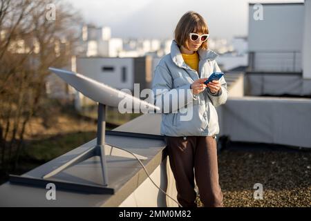 Eine Frau mit Telefon benutzt Starlink-Satelliten-Internet auf dem Dach Stockfoto