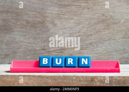Kachelbuchstabe auf rotem Regal in Wort brennt auf Holzhintergrund Stockfoto
