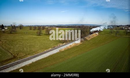 Drohne Blick auf eine antike Dampfmaschine, Annäherung, Dampfblasen und Reisen entlang der Landschaft an einem sonnigen Tag Stockfoto