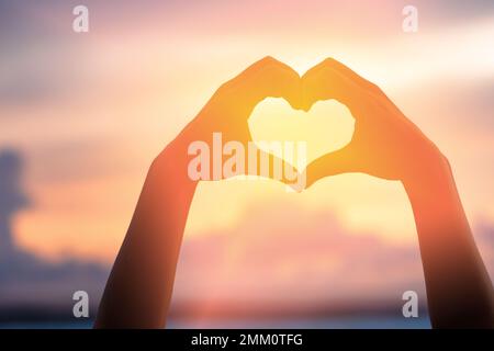 Hände bilden eine Herzform mit Sonnenuntergang Silhouette Stockfoto
