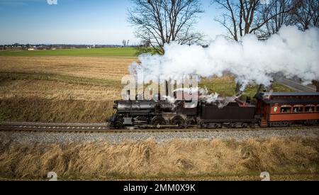 Ein restaurierter antiker Dampferzug, der an einem sonnigen Herbsttag durch die Landschaft reist, aus der Vogelperspektive Stockfoto