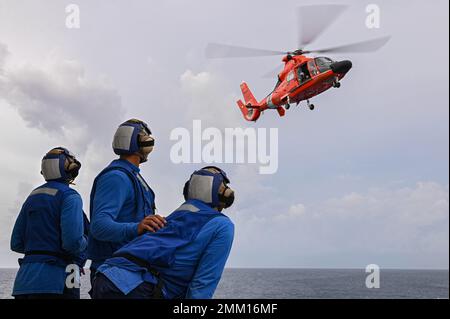 Ein MH-65 Dolphin Hubschrauber aus den USA Coast Guard Air Station Barbers Point nähert sich einer Landung, während Crewmitglieder an Bord von Coast Guard Cutter Midgett (WMSL 757) sich darauf vorbereiten, das Flugzeug nach der Landung am 13. September 2022 festzurren. Die Flugbesatzung und der Hubschrauber werden vorübergehend zur Unterstützung der 2022 Westpazifik-Patrouille eingesetzt. Stockfoto