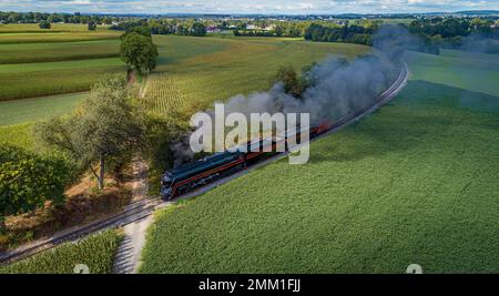 Drohne Blick auf eine antike Dampfmaschine, Annäherung, Dampfblasen und Reisen entlang der Landschaft an einem sonnigen Tag Stockfoto