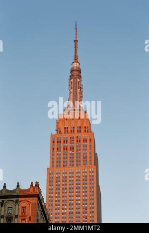 NYC: Die östliche Fassade des Empire State Building verläuft bei Sonnenaufgang von grau bis goldrot, wenn die Sonne am tiefsten Punkt steht. Stockfoto