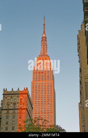 NYC: Die östliche Fassade des Empire State Building verläuft bei Sonnenaufgang von grau bis goldrot, wenn die Sonne am tiefsten Punkt steht. Stockfoto