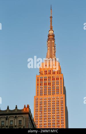 NYC: Die östliche Fassade des Empire State Building verläuft bei Sonnenaufgang von grau bis goldrot, wenn die Sonne am tiefsten Punkt steht. Stockfoto