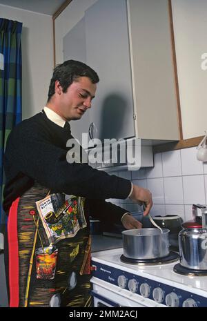 Carl XVI Gustaf, König von Schweden. Geboren am 30. april 1946. Als Kronprinz in seiner Studentenwohnung und Küche, während er in Uppsala studiert. Er steht neben dem Küchenherd und trägt eine Schürze und gibt vor, etwas zu kochen, aber es gibt kein Essen im Kochtopf. 1968 Stockfoto