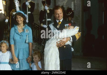 Carl XVI Gustaf, König von Schweden. Geboren am 30. april 1946. Der König Carl XVI. Gustaf hält Prinzessin Madeleine während ihrer Taufe in Slottskyrkan Stockholm am 31. august 1982. Kronprinzessin Victoria, Königin Silvia und Prinz Carl Philip. Stockfoto