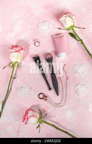 Anordnung aus rosafarbenem Quarzstein Guasha-Schaber, Roller-Massagegerät, Rosen, Schmuck, Kosmetikröhrchen, Pinsel auf Pink. Schönheitspflege für Frauen. Valentinstag Stockfoto