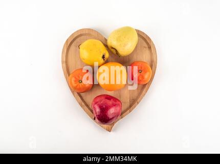 Schüssel mit frischem, reifem Obst auf Holzplatte, weißer Hintergrund isoliert. Reife Mandarine mit voller Schärfentiefe. Frische Orangenapfelquitten für rohe Diät Stockfoto