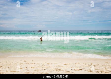 Rückansicht einer brasilianischen Frau, die am Strand Barra da Tijuca in Rio de Janeiro, Brasilien, ins Meer eindringt. Stockfoto