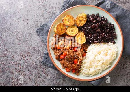 Pabellon Criollo Venezuelas Nationalgericht mit Rinderschredder, Reis, schwarzen Bohnen und gebratenen Kochbananen auf dem Teller auf dem Tisch. Horizontal oben Stockfoto