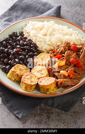 Traditionelles venezolanisches Gericht Pabellon Criollo mit weißem Reis, schwarzen Bohnen, gebratenen Kochbananen und Rinderschredder auf dem Teller. Vertikal Stockfoto