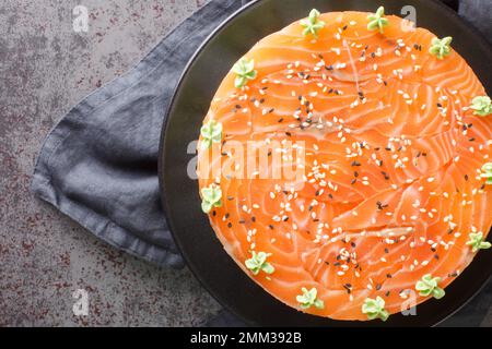 Festlicher Sushi-Kuchen mit rotem Fisch, Reis, Avocado, Frischkäse, Seetang, Sesam ist mit Wasabi-Nahaufnahmen auf einem Teller auf dem Tisch dekoriert. Horizontal t Stockfoto