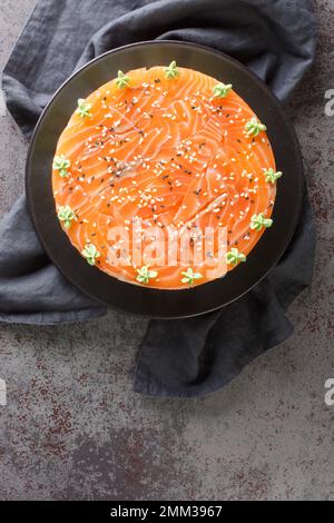 Hausgemachter Sushi-Kuchen mit leicht gesalzenem Lachs, Avocado, Weichkäse und Seetang auf dem Teller auf dem Tisch. Vertikale Draufsicht von oben Stockfoto