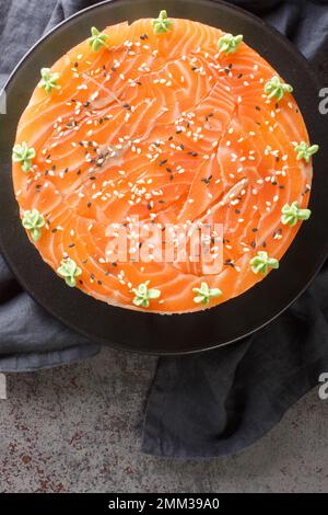 Lachs-Sushi-Kuchen mit Reis, Avocado, Frischkäse, Seetang, Sesamsamen, dekoriert mit Wasabi Nahaufnahme auf einem Teller auf dem Tisch. Vertikale Draufsicht fr Stockfoto