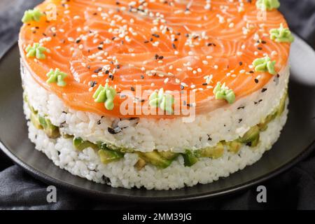 Festlicher Sushi-Kuchen mit rotem Fisch, Reis, Avocado, Frischkäse, Seetang, Sesam ist mit Wasabi-Nahaufnahmen auf einem Teller auf dem Tisch dekoriert. Horizontal Stockfoto