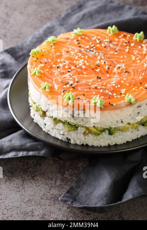 Hausgemachter Sushi-Kuchen mit leicht gesalzenem Lachs, Avocado, Weichkäse und Seetang auf dem Teller auf dem Tisch. Vertikal Stockfoto