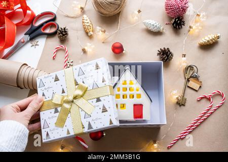 Schlüssel zum Haus mit Schlüsselanhänger auf gemütlichem Zuhause in Geschenkbox mit Weihnachtsdekor-Verpackung. Pack ein Geschenk für Neujahr, Weihnachten. Gebäude, Projekt, Umzug nach Stockfoto