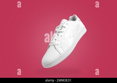 Ansicht des weißen Turnschuhs aus einem großen Winkel auf magentafarbenem (Viva Magenta) Hintergrund. Sportliches Paar Schuhe für Mockup. Modisch, stylisch, sportlich und lässig. Stockfoto
