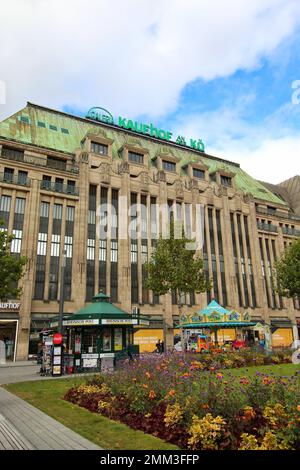 Weitwinkelblick auf das historische Gebäude „Kaufhof an der Kö“ mit Zeitungskiosk und Karussell vor dem Hotel. Galeria Kaufhof ist eine deutsche Kaufhauskette. Stockfoto