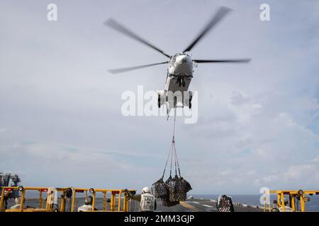 220915-N-XN177-2037 PHILIPPINISCHES MEER (SEPT 15, 2022) – ein AS-332 Super Puma-Hubschrauber liefert während einer Auffüllung auf See mit dem Militärischen Sealift Command Trockenfracht- und Munitionsschiff USNS Carl Brashear (T-AKE 7) am 15. September 2022 eine Ladung an den amphibischen Angriffsträger USS Tripoli (LHA 7). Tripolis ist im Einsatzgebiet der US-Flotte von 7. tätig, um die Interoperabilität mit Verbündeten und Partnern zu verbessern und als einsatzbereite Einsatztruppe für den Frieden und die Stabilität in der Region Indo-Pazifik zu dienen. Stockfoto