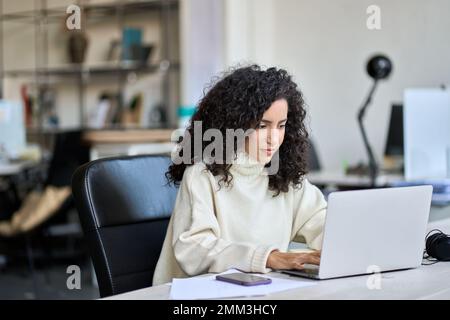Junge lateinische Geschäftsfrau, die am Schreibtisch sitzt und an einem Laptop arbeitet. Stockfoto