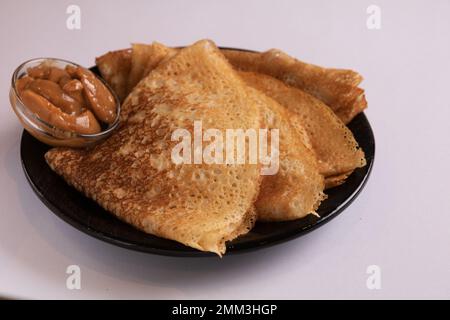 Dünne, feine Pfannkuchen in Dreiecken und abgekochte Kondensmilch auf einer schwarzen Platte Stockfoto