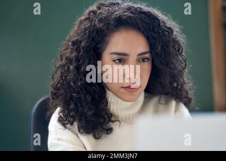 Junge Geschäftsfrau, die sich ein Notebook ansieht und ein Online-Webinar bei der Arbeit ansieht. Stockfoto
