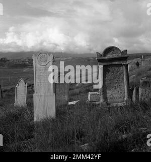 Überreste eines jüdischen Friedhofs in Jelšava, Slowakei. Konzentrieren Sie sich auf alte Grabsteine, Magnezitabbaugebiet im verschwommenen Hintergrund. Aufnahme mit einer analogen 6x6-Kamera. Stockfoto