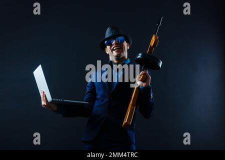 Geschäftsmann in Sonnenbrille mit Maschinengewehr und Laptop Stockfoto