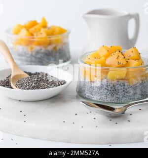 Zwei Chia-Pudding-Parfaits mit gewürfelten Mangos und einer Schüssel Chiasamen. Stockfoto
