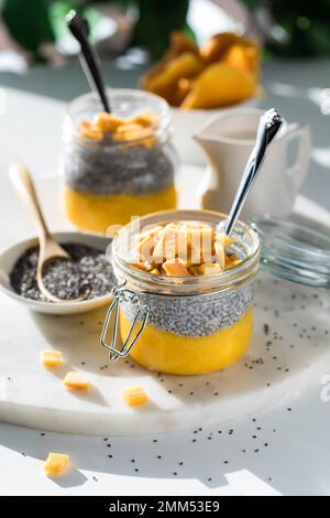 Pürierte Mango Chia Pudding Snacks auf einer Marmorplatte auf einem Tisch in hellem Sonnenlicht. Stockfoto