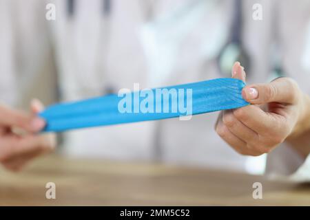 Physiotherapeutin zeigt blaue medizinische Klebebänder in den Händen, während sie am Tisch in der medizinischen Klinik sitzt. Stockfoto