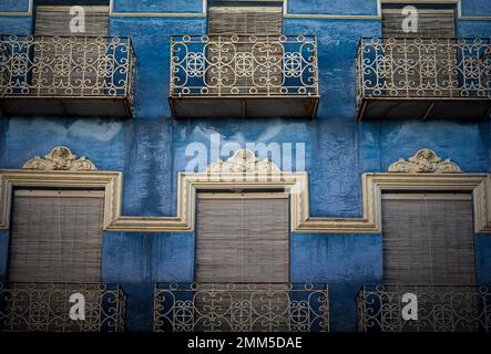 Die Fassade des alten Gebäudes besteht aus dunkelblauen Fenstern mit Fensterläden, schmiedeeisernen Balkonen und dekorativen weißen Stuckverzierungen Stockfoto