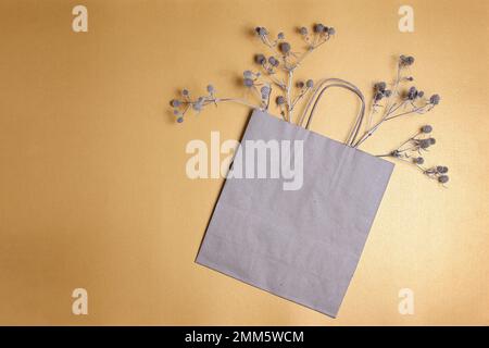 Zusammensetzung mit Papierbeutel und trockenen Stachelpflanzen. Braune Kraftpapiertüte auf goldenem Hintergrund mit Kopierraum. Null-Abfall-Konzept, Draufsicht. Stockfoto