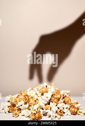 Abstrakte Zusammensetzung. Der Schatten der Hand greift nach Popcorn. Popcorn-Mix, Karamell und gesalzenes Popcorn. Konzentriere dich auf Popcorn. Stockfoto