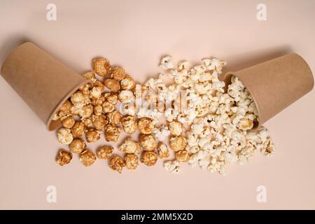 Zwei Arten Popcorn in zwei Pappbechern. Сaramel-gedecktes und gesalzenes Popcorn. Popcorn verschüttete aus den Tassen und mischte sich. Geringe Schärfentiefe, Draufsicht. Stockfoto