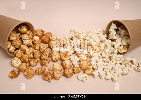 Zwei Arten Popcorn in zwei Pappbechern. Сaramel-gedecktes und gesalzenes Popcorn. Popcorn verschüttete aus den Tassen und mischte sich. Geringe Schärfentiefe. Stockfoto