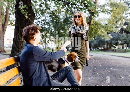 Ein Mann mit einem Beagle begrüßt eine junge Blondine im Park Stockfoto