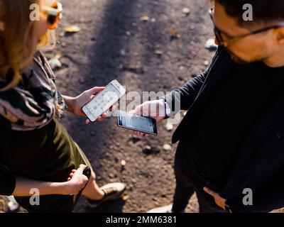 Ein Mann und eine junge Blondine tauschen im Park Telefone aus Stockfoto