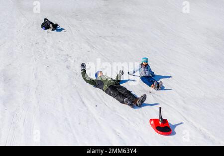 Ein Vater und Kinder fuhren im Winter gemeinsam den schneebedeckten Hügel hinunter Stockfoto