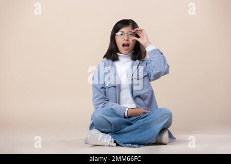Ein mexikanisches Mädchen, das auf dem Boden sitzt und eine Brille trägt, überraschte das Gesicht Stockfoto