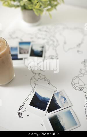 Polaroid-Fotos auf Travel World-Karte mit Eiskaffee und Pflanzen Stockfoto