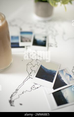 Polaroid-Fotos auf Travel World-Karte mit Eiskaffee und Pflanzen Stockfoto